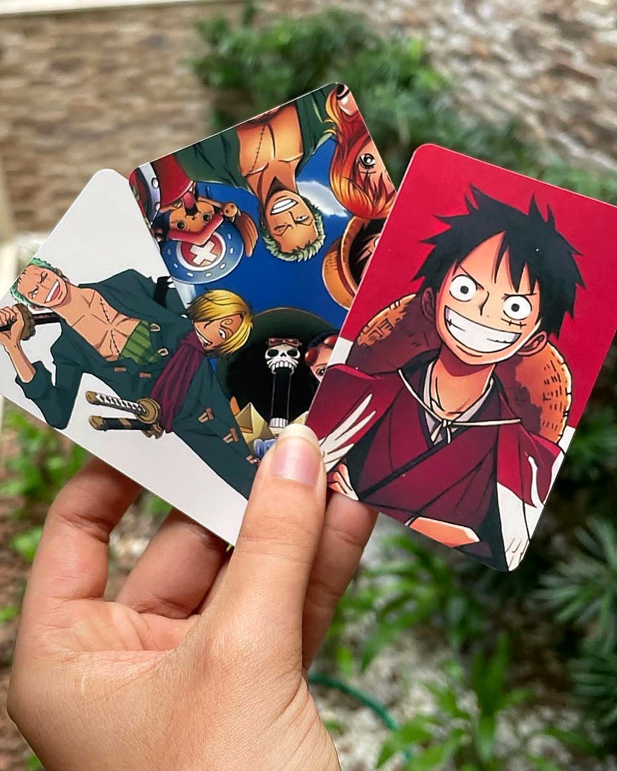 Photocards de One Piece impressos sendo segurados na mão